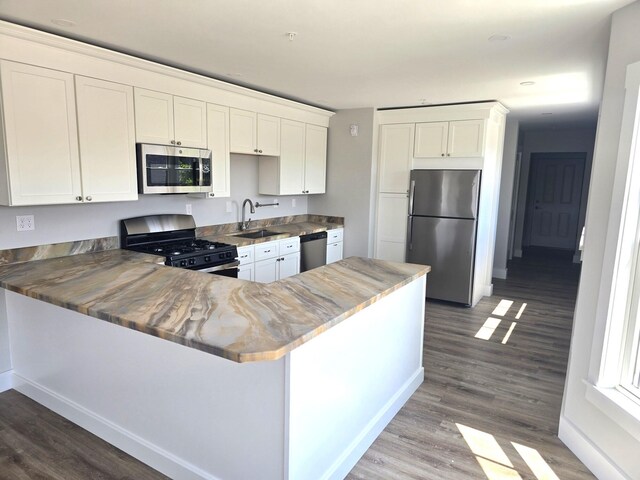 106 Cumberland Ave Unit 201, Portland, ME 04101 - kitchen with appliances with stainless steel finishes, wood finished floors, white cabinets, and a peninsula