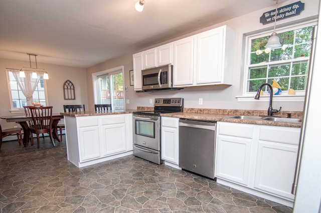 9 St James Pl, Lewiston, ME 04240 - kitchen with appliances with stainless steel finishes, a peninsula, white cabinetry, dark stone finish flooring, and decorative light fixtures