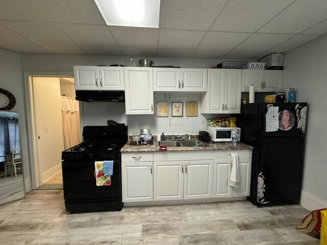 46 Cedar St, Dover-Foxcroft, ME 04426 - kitchen featuring black appliances, under cabinet range hood, a paneled ceiling, white cabinetry, and light wood-style flooring