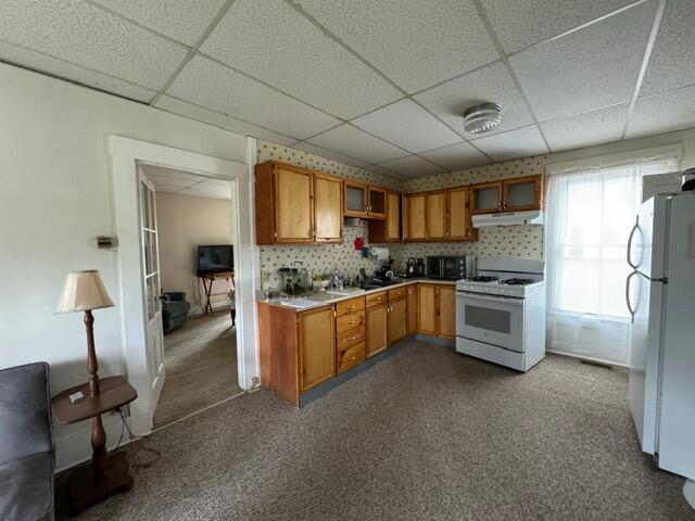 46 Cedar St, Dover-Foxcroft, ME 04426 - kitchen with white appliances, under cabinet range hood, a paneled ceiling, brown cabinetry, and light countertops