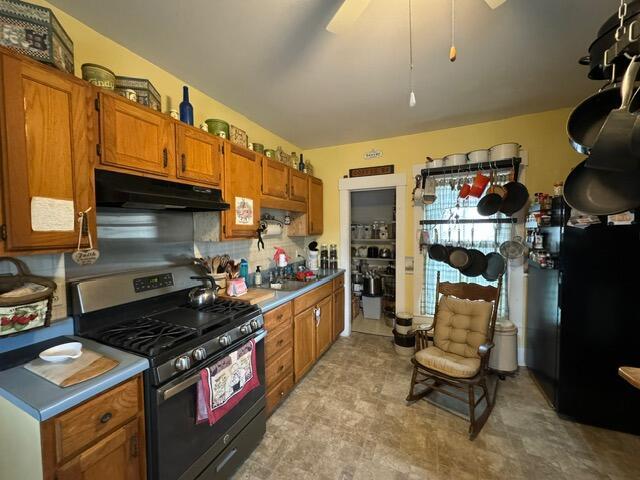 46 Cedar St, Dover-Foxcroft, ME 04426 - kitchen featuring stainless steel range with gas cooktop, under cabinet range hood, decorative backsplash, brown cabinets, and light countertops