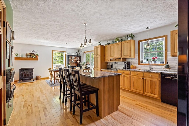 34 Cari Way, Sidney, ME 04330 - kitchen featuring black dishwasher, a textured ceiling, a wood stove, light wood-style flooring, and dark stone counters