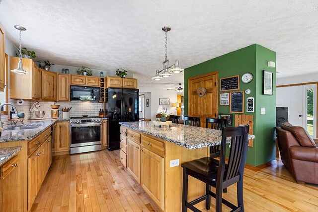 34 Cari Way, Sidney, ME 04330 - kitchen with black appliances, light wood-type flooring, a textured ceiling, a kitchen island, and a breakfast bar area