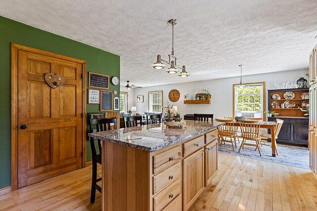 34 Cari Way, Sidney, ME 04330 - kitchen with light wood-type flooring, a breakfast bar, a textured ceiling, a center island, and dark stone countertops