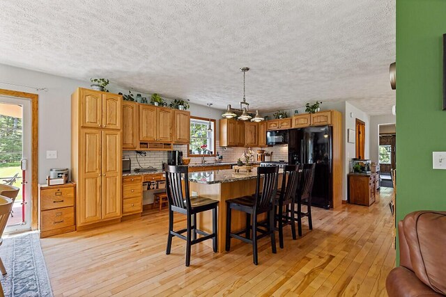 34 Cari Way, Sidney, ME 04330 - kitchen with black appliances, light wood-style flooring, backsplash, a breakfast bar area, and a textured ceiling
