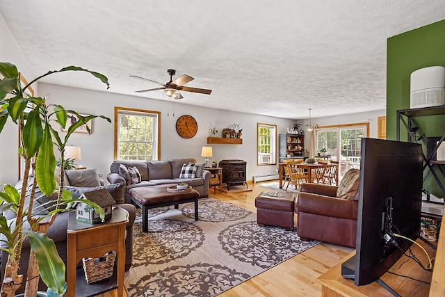 34 Cari Way, Sidney, ME 04330 - living area featuring a wood stove, a textured ceiling, a baseboard heating unit, wood finished floors, and a ceiling fan