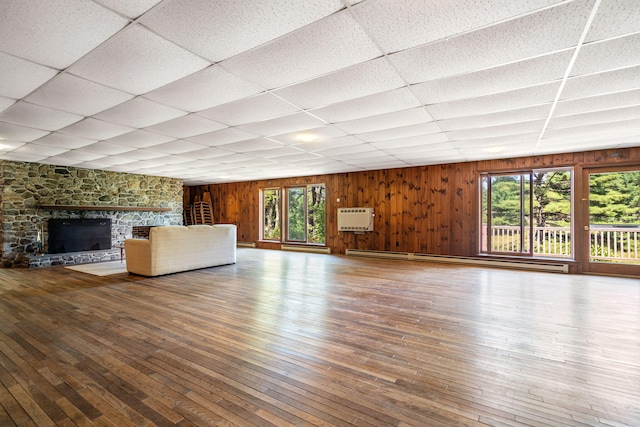 unfurnished living room featuring a baseboard radiator, healthy amount of natural light, wood-type flooring, a drop ceiling, and wood walls