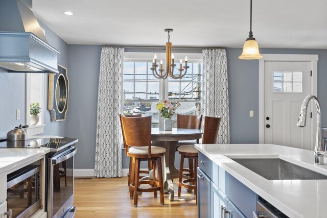 38 Atlantic Ave, Boothbay Harbor, ME 04538 - kitchen with wall chimney range hood, light wood-style floors, appliances with stainless steel finishes, a chandelier, and healthy amount of natural light
