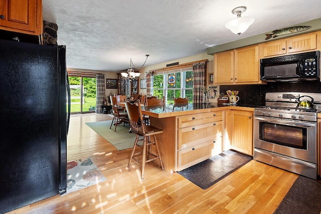 1 Castle View Ln, Belgrade, ME 04917 - kitchen with black appliances, a peninsula, light wood-style flooring, a chandelier, and a kitchen bar