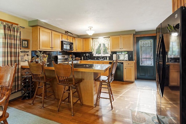 1 Castle View Ln, Belgrade, ME 04917 - kitchen featuring black appliances, light wood-style flooring, a peninsula, backsplash, and a kitchen breakfast bar