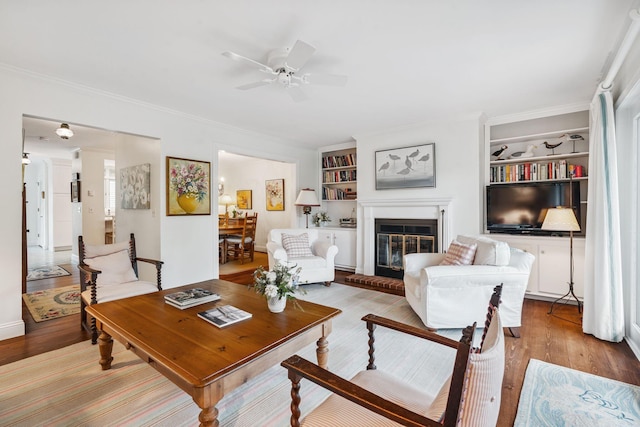 239 Sea Rd Unit 32, Kennebunk, ME 04043 - living room featuring built in features, wood finished floors, a glass covered fireplace, ceiling fan, and crown molding