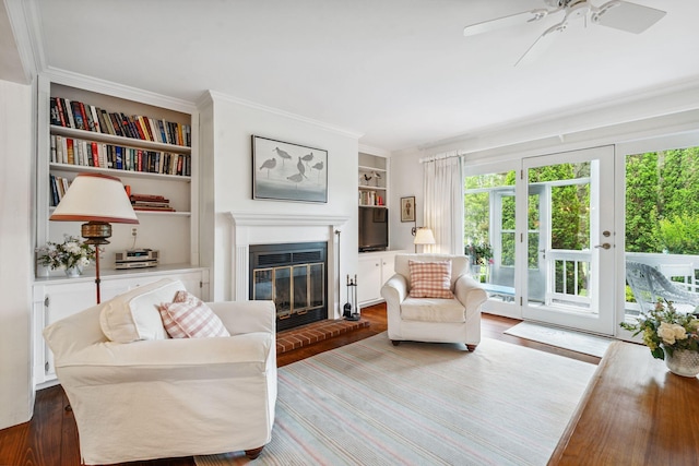 239 Sea Rd Unit 32, Kennebunk, ME 04043 - living room featuring built in features, wood finished floors, a glass covered fireplace, a ceiling fan, and crown molding