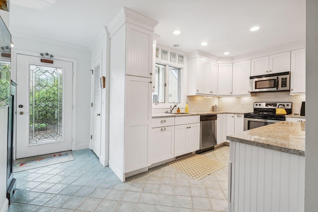 239 Sea Rd Unit 32, Kennebunk, ME 04043 - kitchen with appliances with stainless steel finishes, crown molding, white cabinets, tasteful backsplash, and light stone countertops