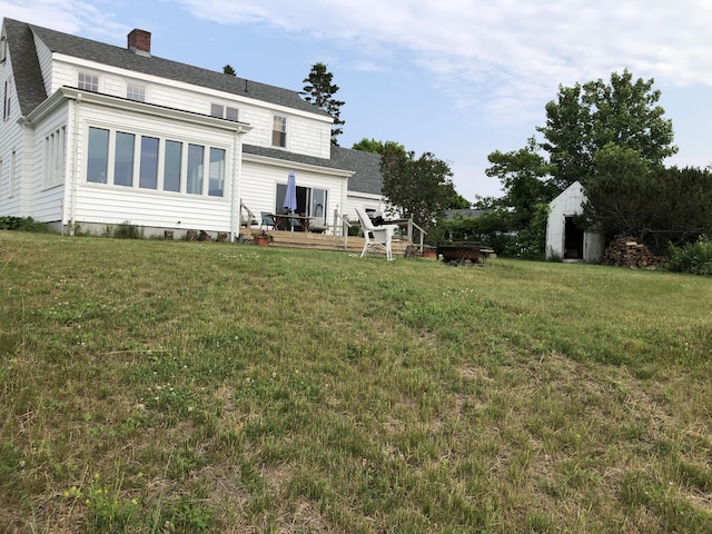 95 Main St, Lubec, ME 04652 - rear view of property featuring a wooden deck, a lawn, a shingled roof, and a chimney