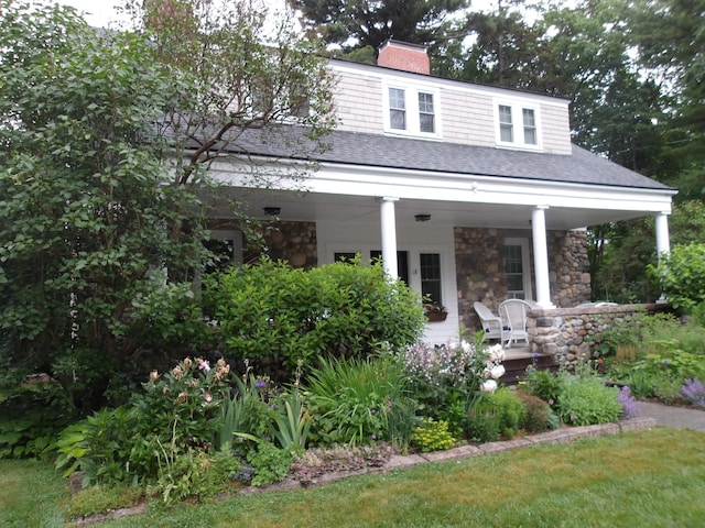 18 Wayman Ln, Bar Harbor, ME 04609 - view of front facade with stone siding, covered porch, a shingled roof, and a chimney