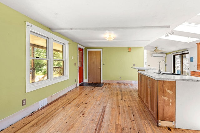 276 W St, Biddeford, ME 04005 - kitchen with light wood-style floors, brown cabinets, light countertops, an AC wall unit, and a kitchen island with sink