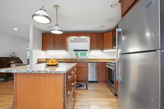 17 Beryl Loop Unit F65, Topsham, ME 04086 - kitchen featuring stainless steel appliances, brown cabinetry, a center island, light wood-style flooring, and light stone countertops