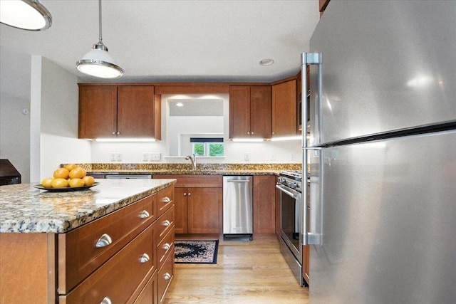 17 Beryl Loop Unit F65, Topsham, ME 04086 - kitchen with appliances with stainless steel finishes, brown cabinets, light wood finished floors, light stone countertops, and pendant lighting