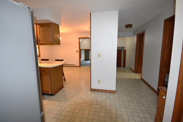 94 Blaisdell Rd, Newport, ME 04953 - kitchen featuring freestanding refrigerator, light countertops, a baseboard heating unit, light tile patterned floors, and brown cabinets