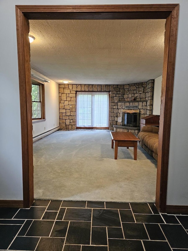 94 Blaisdell Rd, Newport, ME 04953 - unfurnished living room featuring dark colored carpet, a baseboard heating unit, a stone fireplace, and a textured ceiling