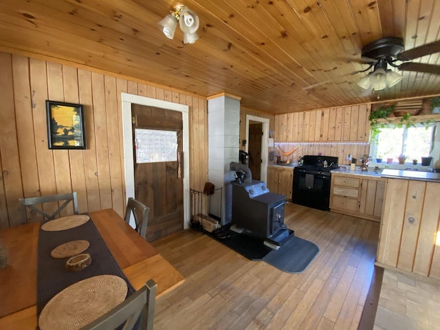 6 Chicken St, Starks, ME 04911 - kitchen with light brown cabinets, black range oven, a wood stove, wooden walls, and a ceiling fan