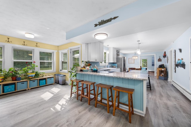 97 Forest Ave, Orono, ME 04473 - kitchen featuring stainless steel fridge, light wood-type flooring, a peninsula, light stone countertops, and a breakfast bar