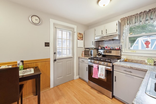 119 Falvey St, Bangor, ME 04401 - kitchen featuring stainless steel appliances, under cabinet range hood, light wood-style flooring, a wainscoted wall, and white cabinetry