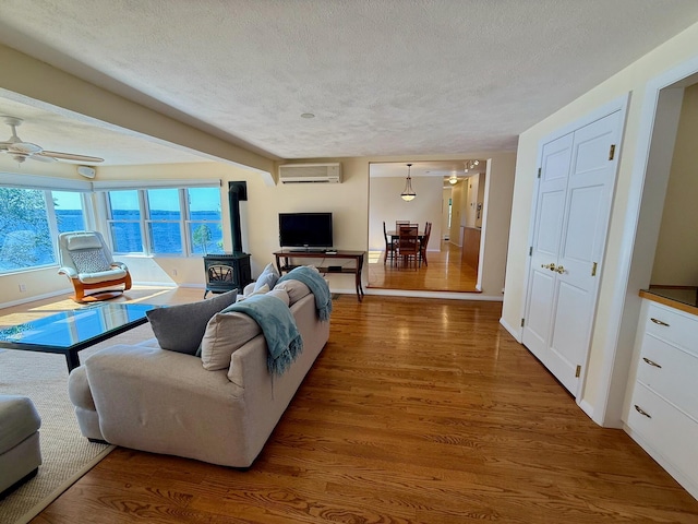 48 Sheltons Rd, Trenton, ME 04605 - living area with a wood stove, a wall unit AC, a textured ceiling, wood finished floors, and a ceiling fan