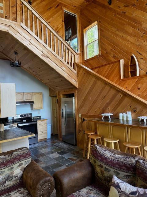 24 Cliffside Dr, Saint Albans, ME 04971 - living area with high vaulted ceiling, wood walls, dark stone finish flooring, and stairway
