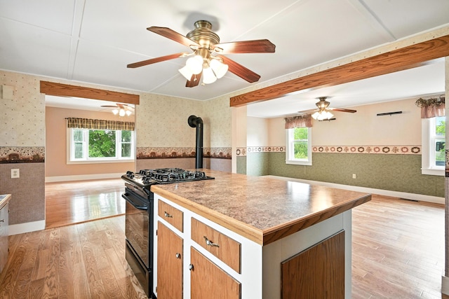23 W St, Benton, ME 04901 - kitchen with wallpapered walls, a wood stove, black gas range oven, open floor plan, and a wainscoted wall