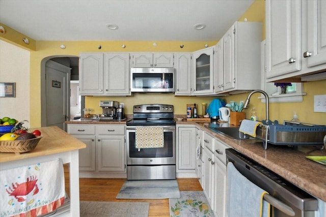 278 S Main St, Auburn, ME 04210 - kitchen featuring appliances with stainless steel finishes, light wood finished floors, arched walkways, white cabinetry, and glass insert cabinets