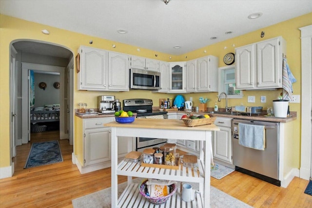 278 S Main St, Auburn, ME 04210 - kitchen with stainless steel appliances, white cabinetry, light wood-type flooring, glass insert cabinets, and arched walkways