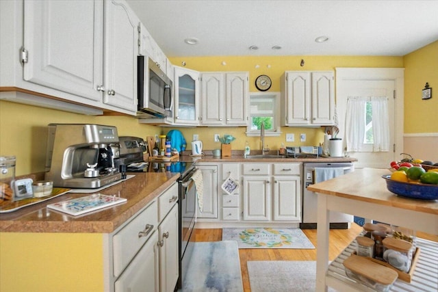 278 S Main St, Auburn, ME 04210 - kitchen with appliances with stainless steel finishes, light wood-style floors, white cabinetry, glass insert cabinets, and recessed lighting