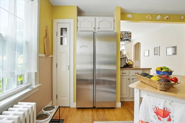 278 S Main St, Auburn, ME 04210 - kitchen featuring freestanding refrigerator, radiator, white cabinets, light wood finished floors, and arched walkways