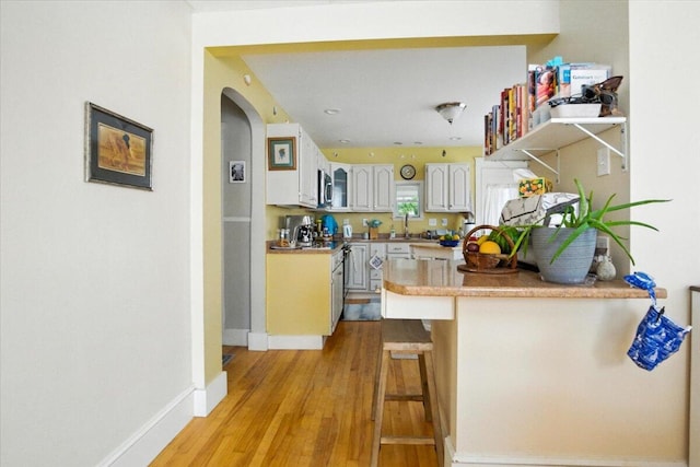 278 S Main St, Auburn, ME 04210 - kitchen featuring a peninsula, arched walkways, light wood-style flooring, stainless steel microwave, and light countertops