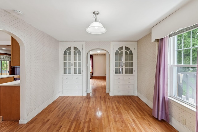 15 Huston Ave, Auburn, ME 04210 - unfurnished dining area featuring arched walkways, wallpapered walls, and light wood-style flooring