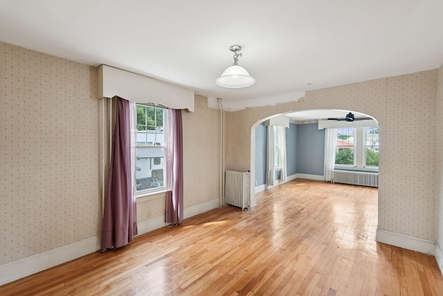 15 Huston Ave, Auburn, ME 04210 - spare room featuring radiator heating unit, arched walkways, wood finished floors, and wallpapered walls