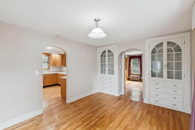15 Huston Ave, Auburn, ME 04210 - unfurnished dining area featuring arched walkways, light wood-style floors, radiator, and wallpapered walls