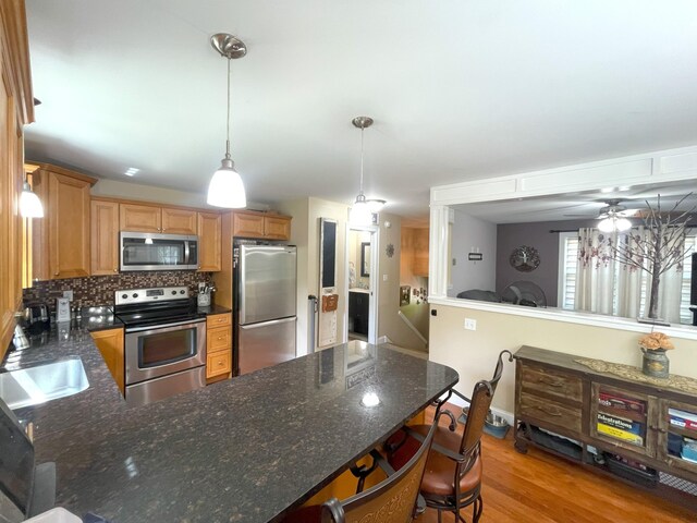28 Kayla Way, Gorham, ME 04038 - kitchen featuring appliances with stainless steel finishes, a peninsula, decorative backsplash, hanging light fixtures, and light wood-style flooring