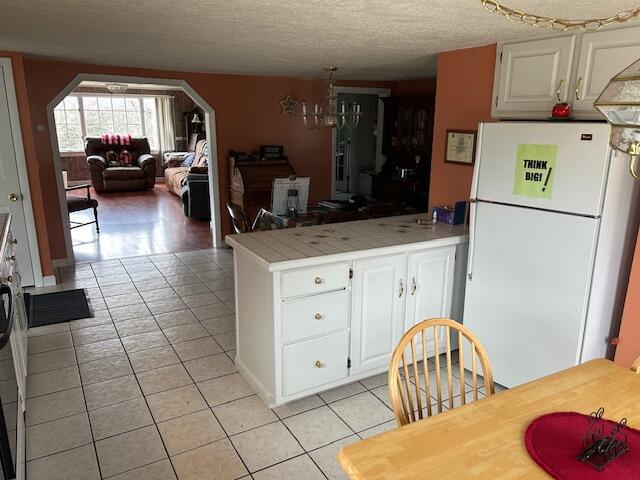 1039 Belfast Rd, Knox, ME 04986 - kitchen with freestanding refrigerator, a peninsula, light tile patterned flooring, white cabinetry, and light countertops