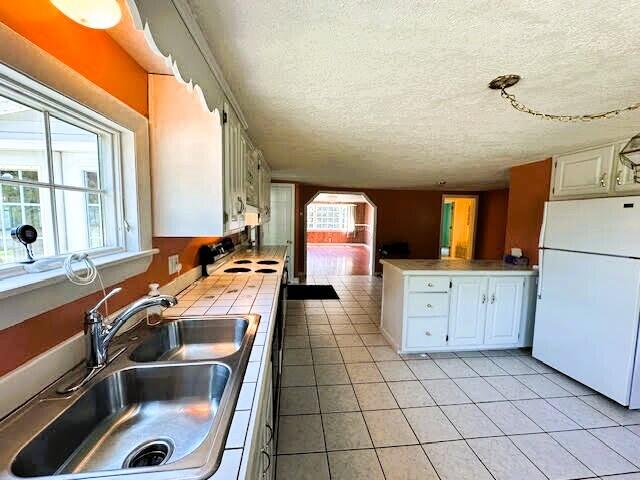 1039 Belfast Rd, Knox, ME 04986 - kitchen featuring freestanding refrigerator, tile countertops, a textured ceiling, light tile patterned flooring, and white cabinets