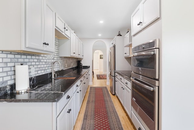 29 Folly Farm Rd, Lebanon, ME 04027 - kitchen with stainless steel appliances, arched walkways, light wood finished floors, backsplash, and dark stone countertops