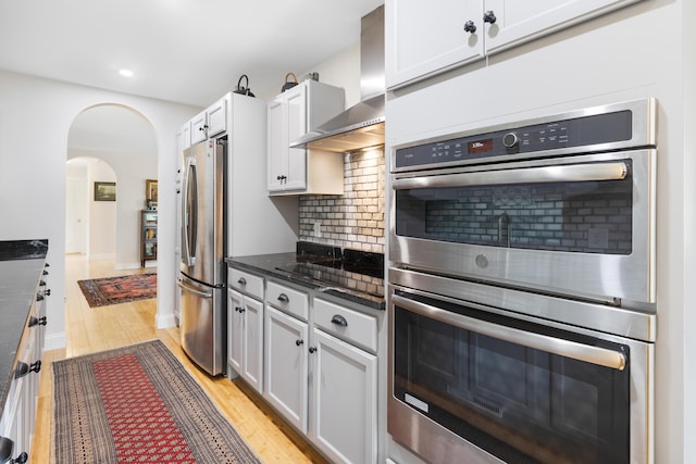 29 Folly Farm Rd, Lebanon, ME 04027 - kitchen featuring wall chimney exhaust hood, appliances with stainless steel finishes, arched walkways, light wood-style flooring, and decorative backsplash
