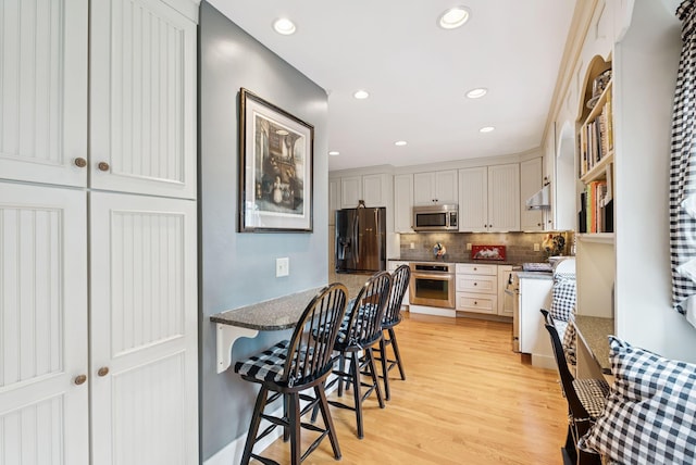 709 High St, Bath, ME 04530 - kitchen with appliances with stainless steel finishes, light wood finished floors, a breakfast bar, decorative backsplash, and recessed lighting
