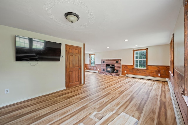 24 Blackswoods Rd, Franklin, ME 04634 - unfurnished living room featuring baseboard heating, light wood finished floors, a wainscoted wall, a brick fireplace, and wooden walls