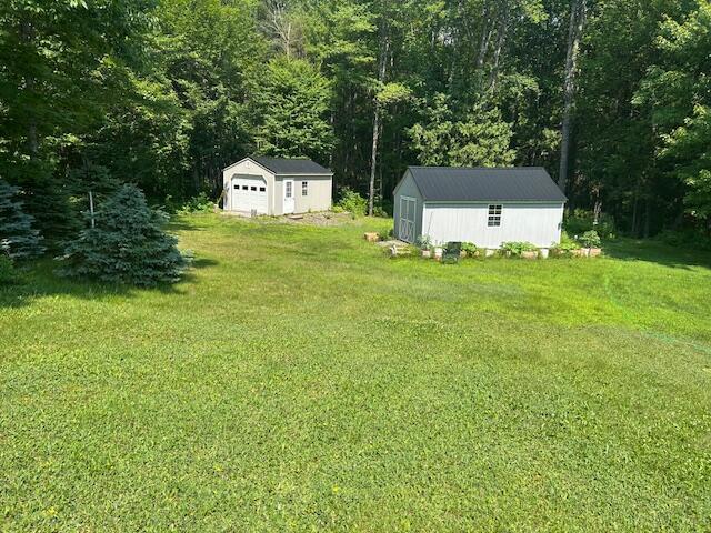 60 Dawes Rd, Dover-Foxcroft, ME 04426 - view of grassy yard featuring an outbuilding, a detached garage, and a view of trees