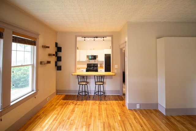 99 Gamage Ave, Auburn, ME 04210 - kitchen with black appliances, wood finished floors, white cabinets, rail lighting, and a kitchen breakfast bar