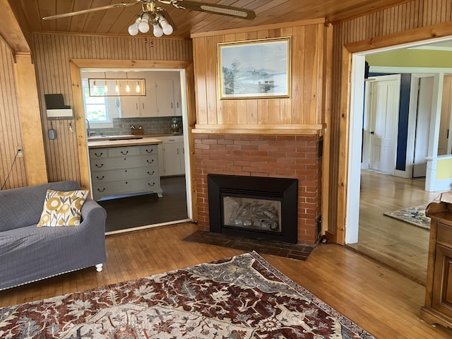 16 N Main St, Morrill, ME 04952 - living room with wood-type flooring, wood walls, a ceiling fan, wooden ceiling, and a brick fireplace