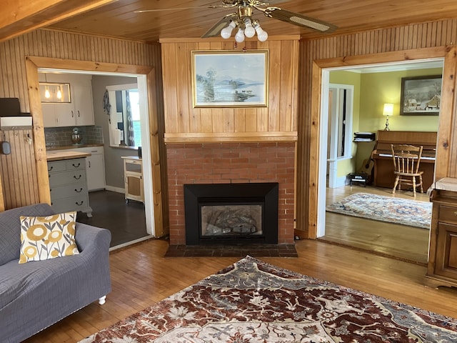 16 N Main St, Morrill, ME 04952 - living room with wood-type flooring, a ceiling fan, wooden walls, and a brick fireplace