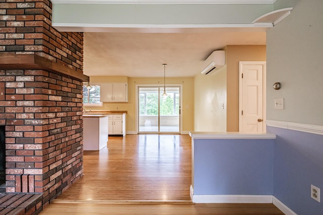 704 Brighton Hill Rd, Minot, ME 04258 - kitchen featuring a wall mounted AC, white cabinets, light wood-style floors, and hanging light fixtures